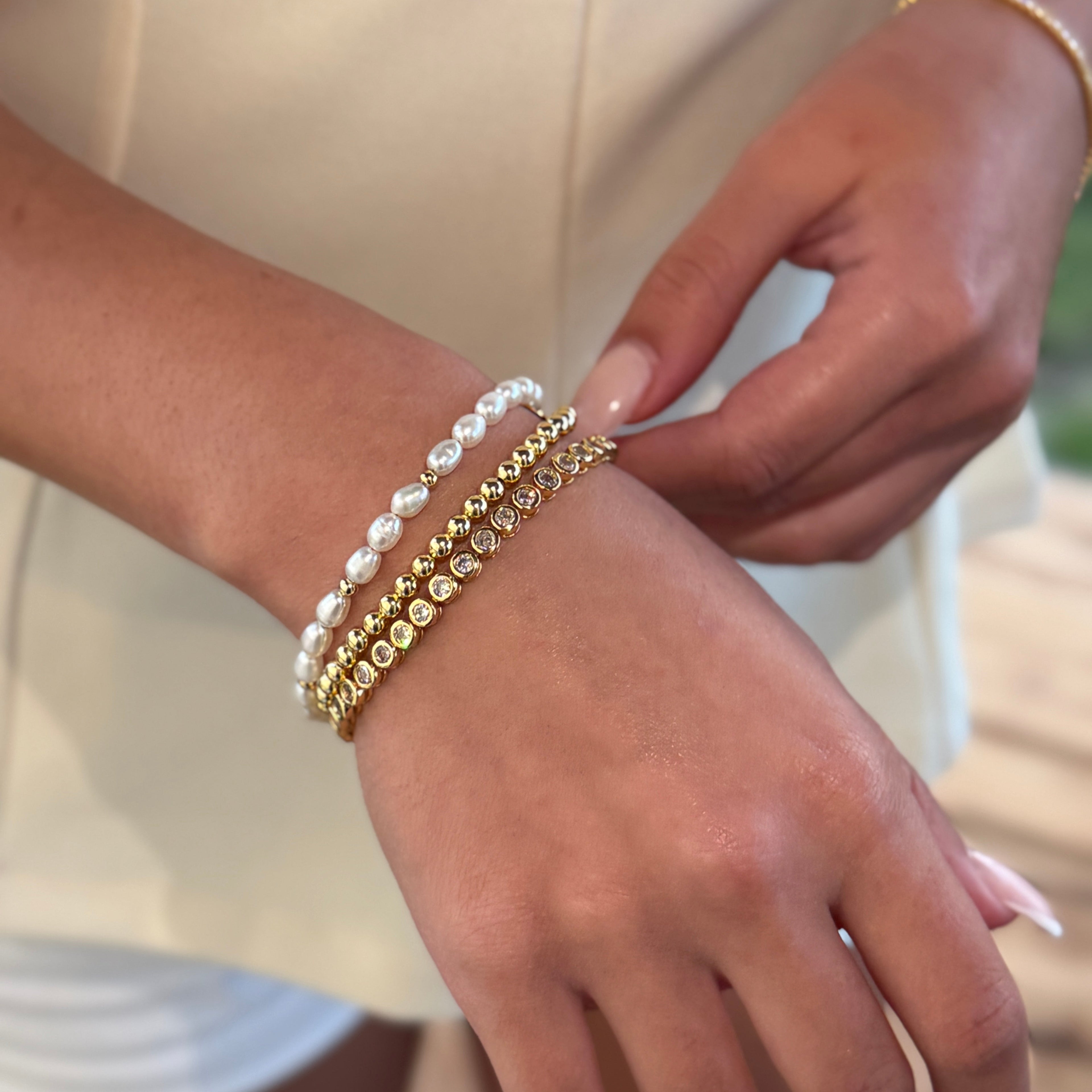 Close-up of a hand wearing multiple gold bracelets with a blurred background