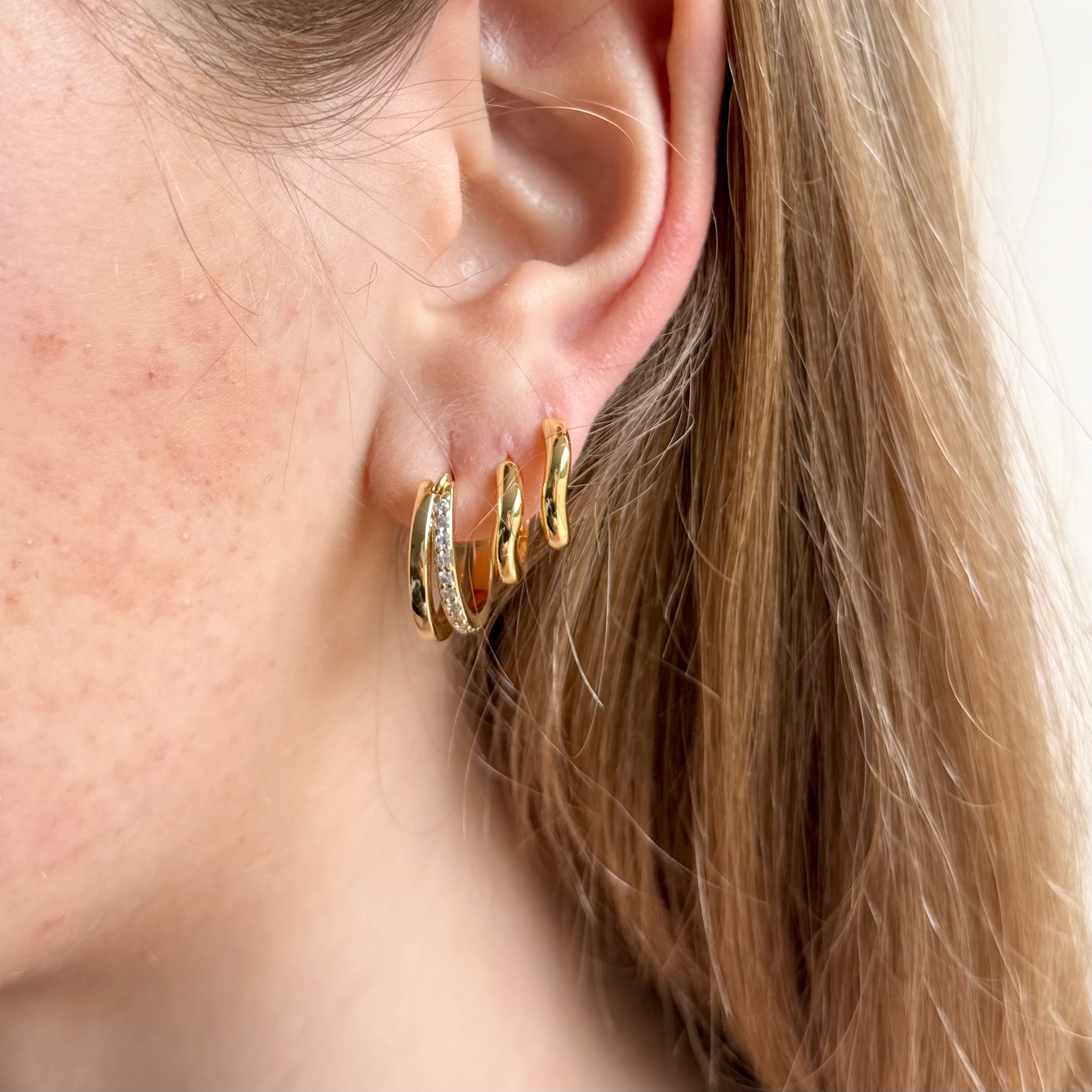 Gold slim wave huggie earrings worn by model, minimalist and modern