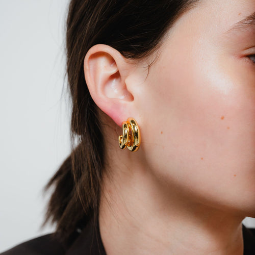 Close-up of a person wearing gold hoop earrings with a neutral background