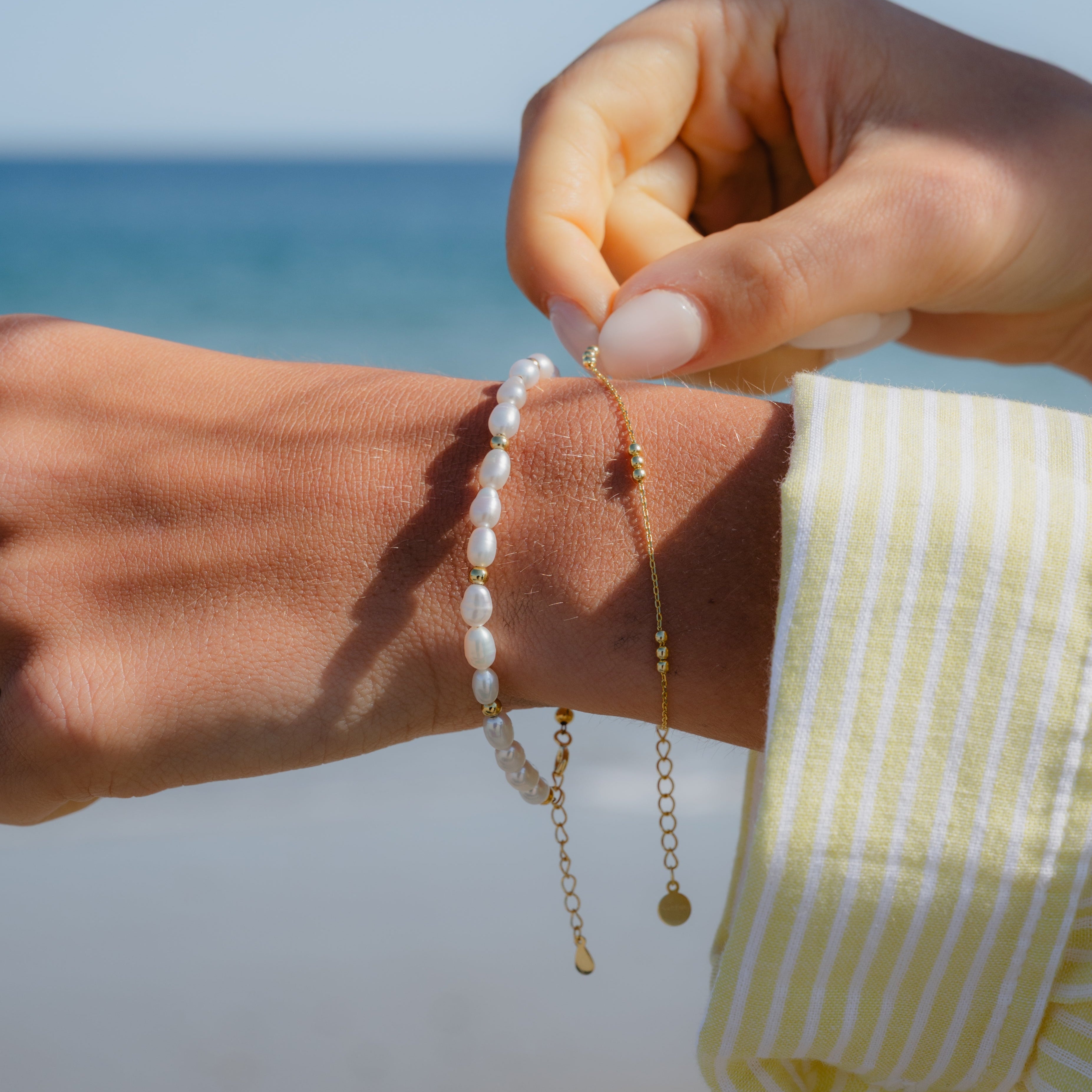 Dainty gold bead bracelet styled on wrist, layered with other bracelets