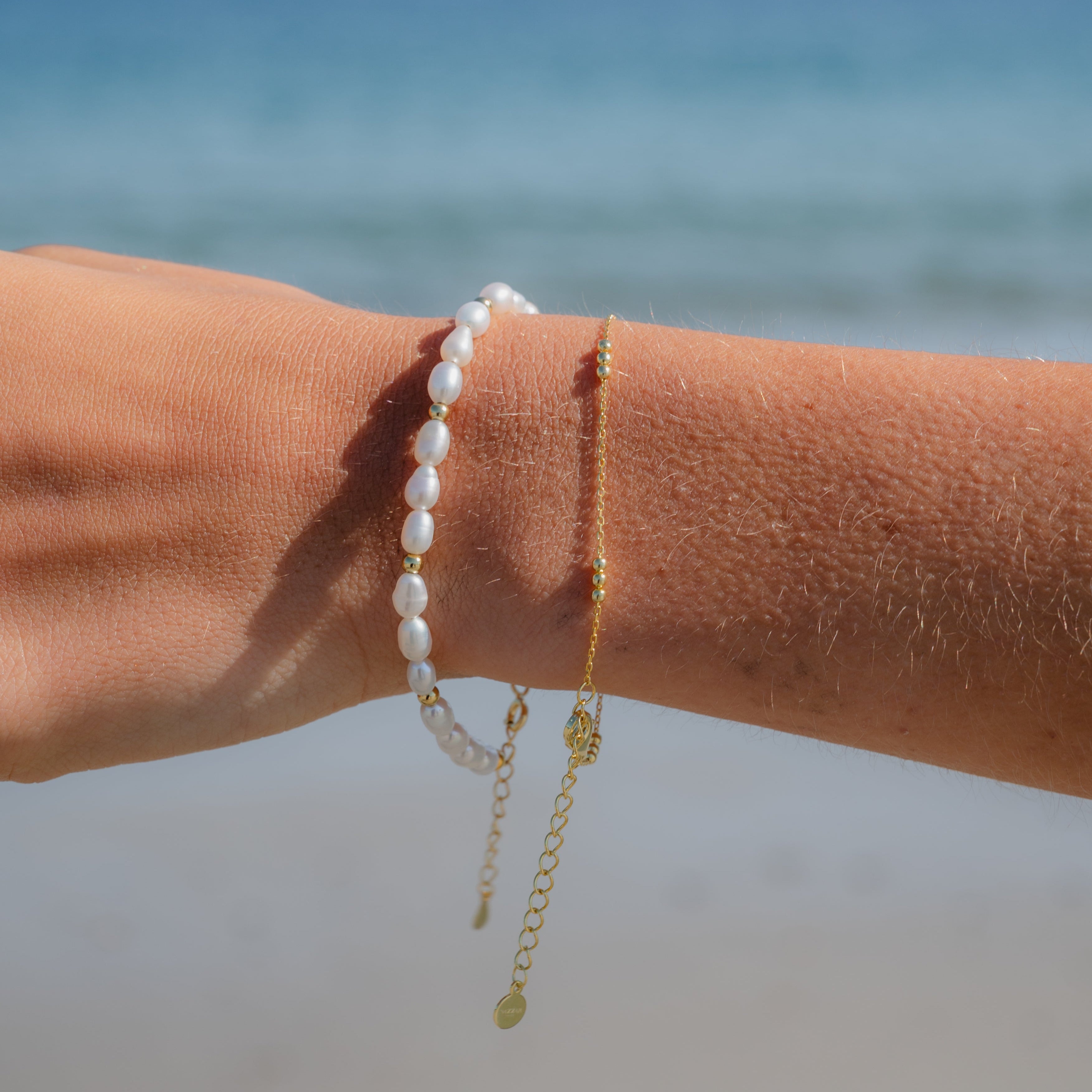 Delicate freshwater pearl and gold bracelet layered with other jewelry on model’s arm

