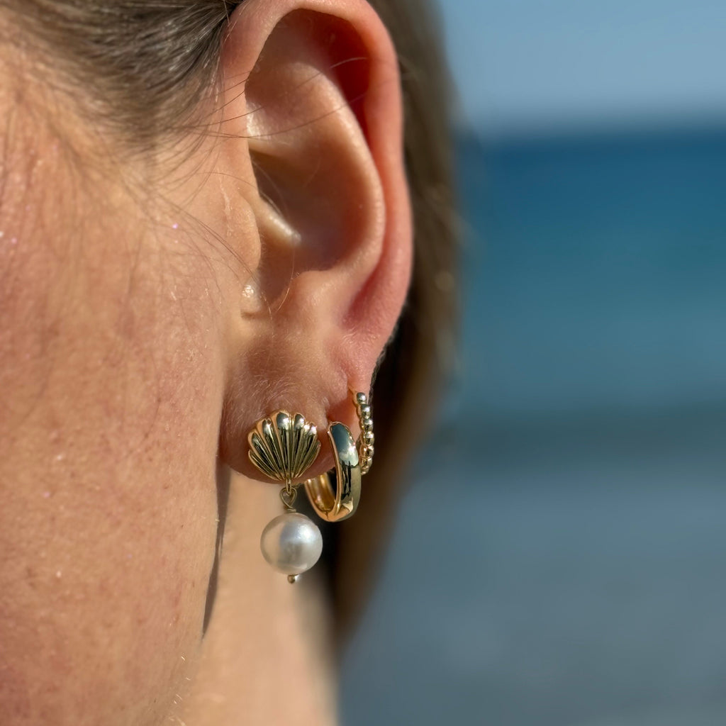 Stacked gold earrings worn on model’s ear, mixing hoops and studs for a trendy look