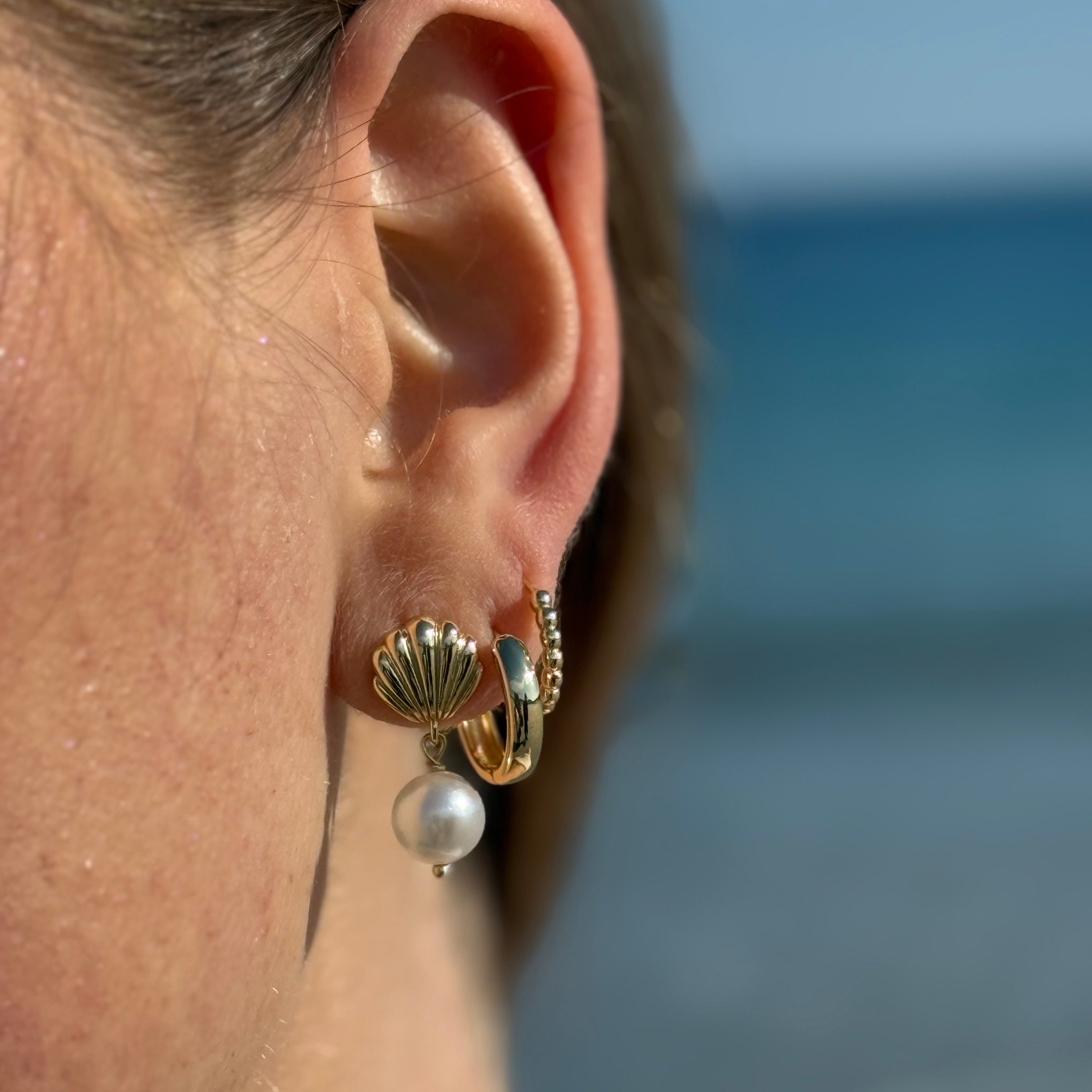 Stacked gold earrings worn on model’s ear, mixing hoops and studs for a trendy look